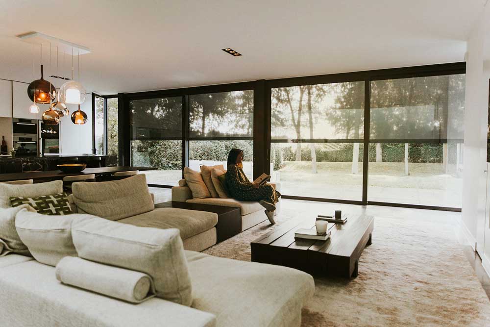 Kvinne står ved gulv-til-tak-vindu med screen som slipper inn naturlig lys